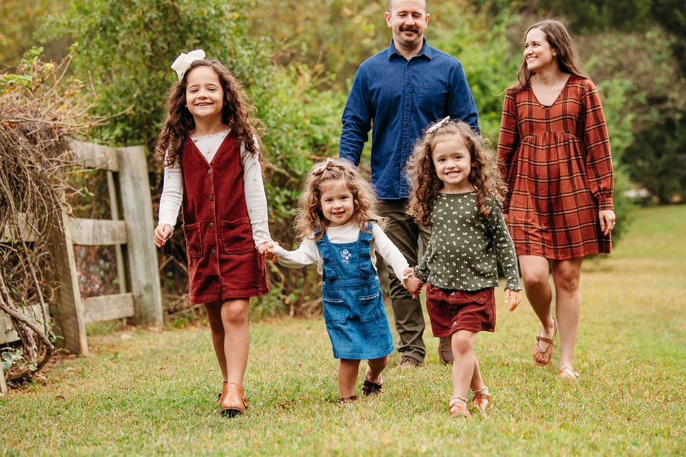 Joyful family of five walking together through a grassy field on a sunny day.