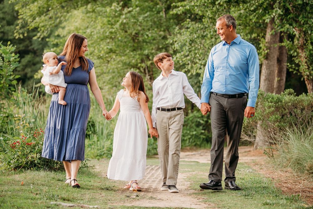 Happy family of five walking hand in hand along a scenic garden path in summer.