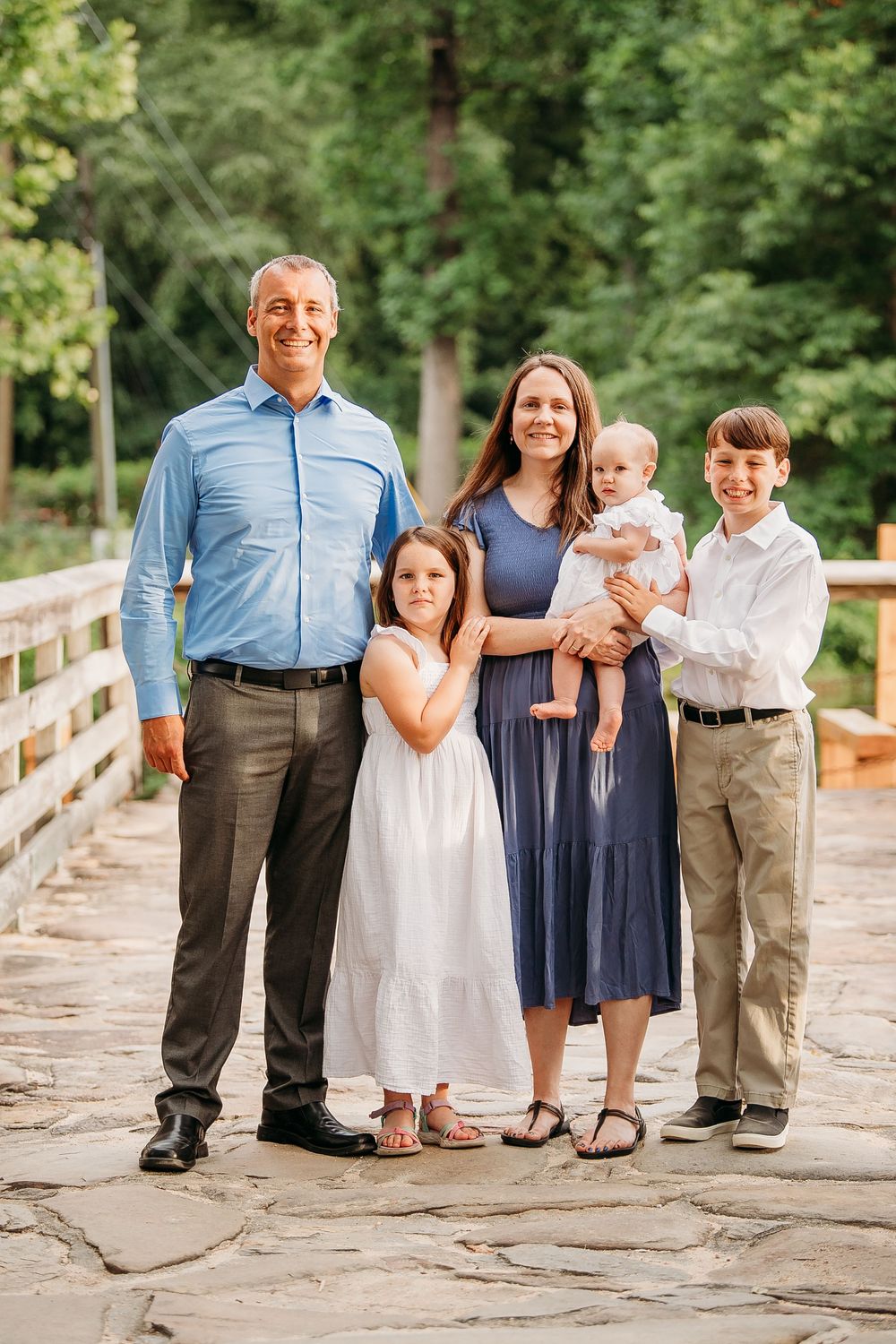 Family of five posing on stone bridge surrounded by lush green trees during outdoor photo session.