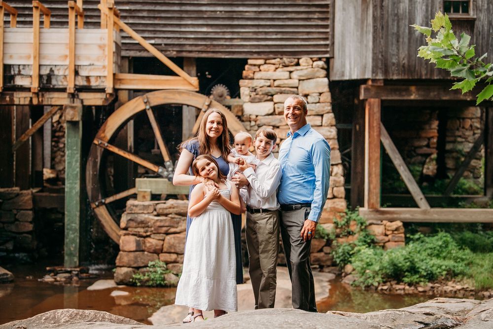Family of five posing together in front of a rustic old water mill in nature.