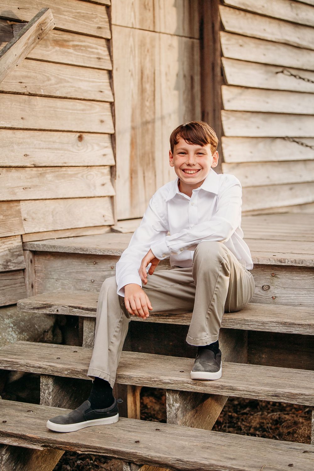 Smiling young boy in white shirt and khaki pants sitting on wooden steps outdoors.
