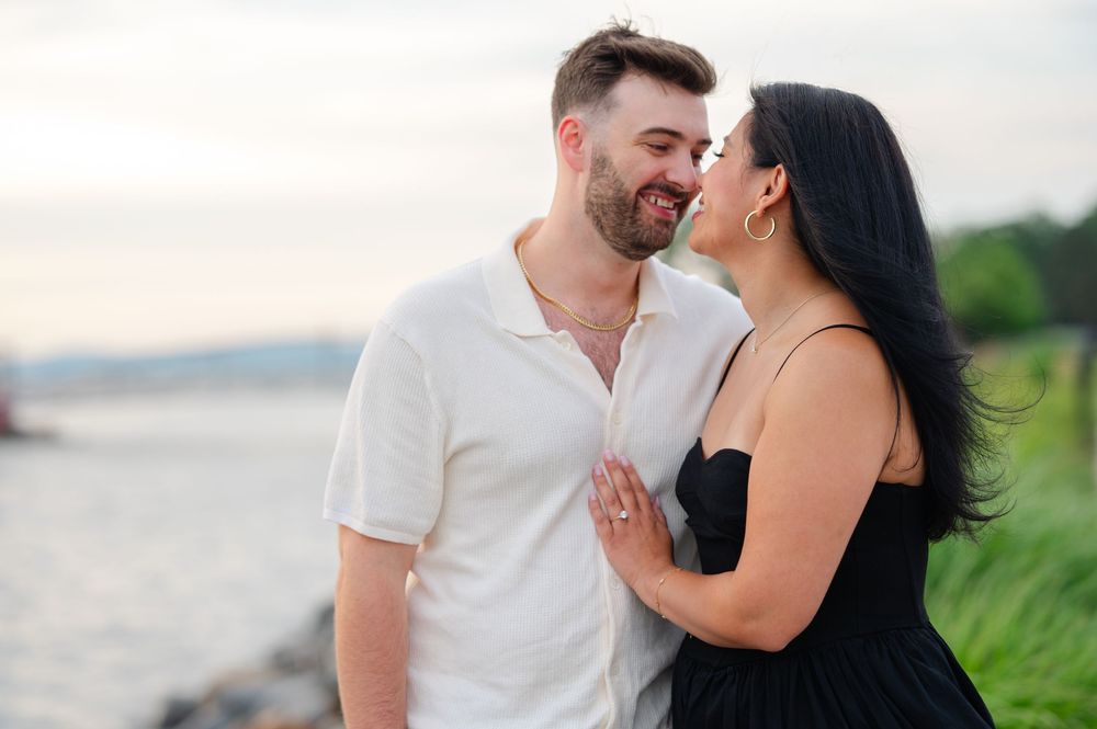 Happy couple smiling and holding hands near a waterfront at golden hour.