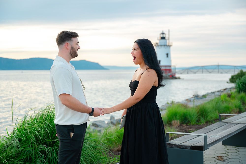 Couple holding hands smiling at each other by a lighthouse on the Hudson River at sunset.