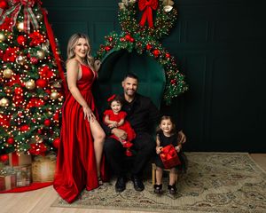 Family of four in red and black outfits posing by a decorated Christmas tree for a festive holiday portrait.