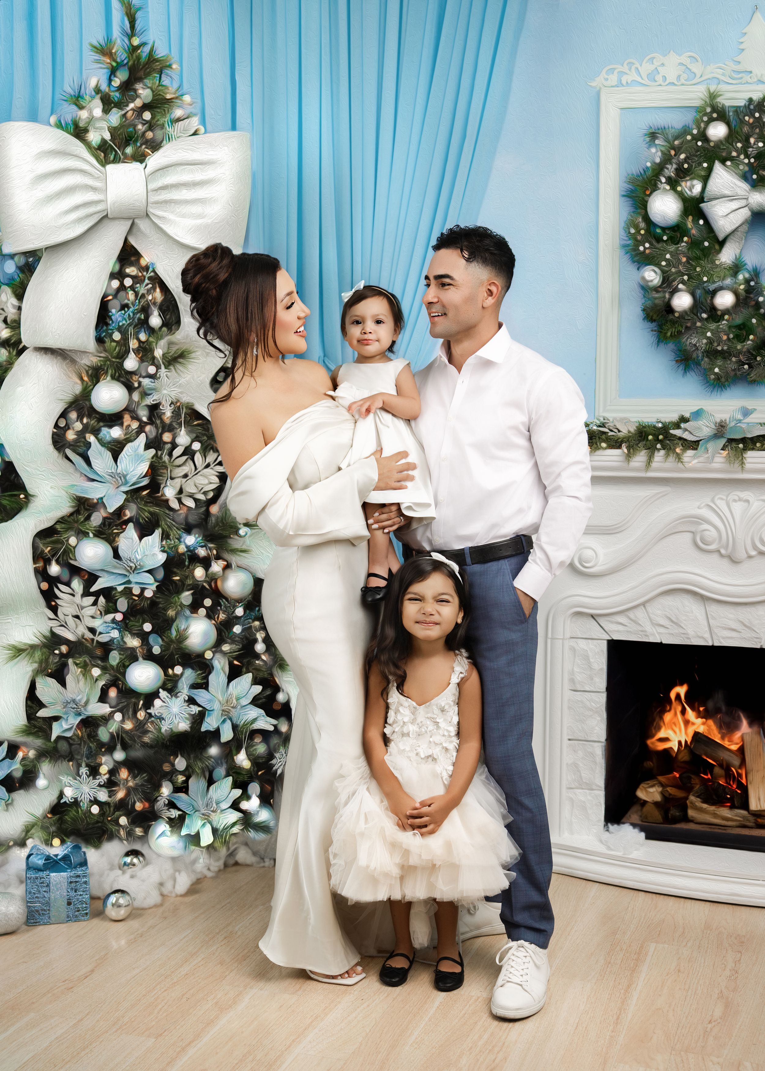 Family of four poses in white outfits by decorated Christmas tree and fireplace in festive blue room.