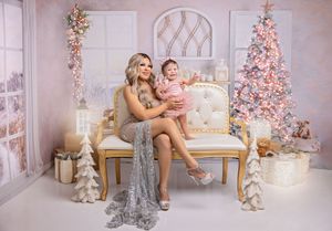 Mother and baby girl in pink and silver outfits pose on gold bench beside decorated Christmas tree.