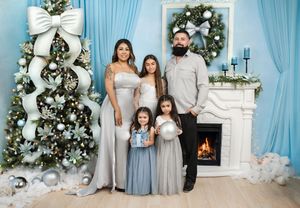 Family of five posing in front of decorated Christmas tree and fireplace in blue and white holiday themed room.