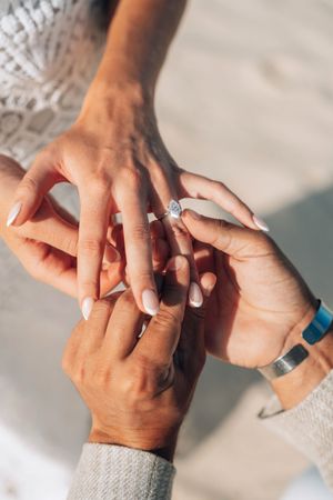 Close-up of a person placing a diamond engagement ring on their partner's finger during a proposal.