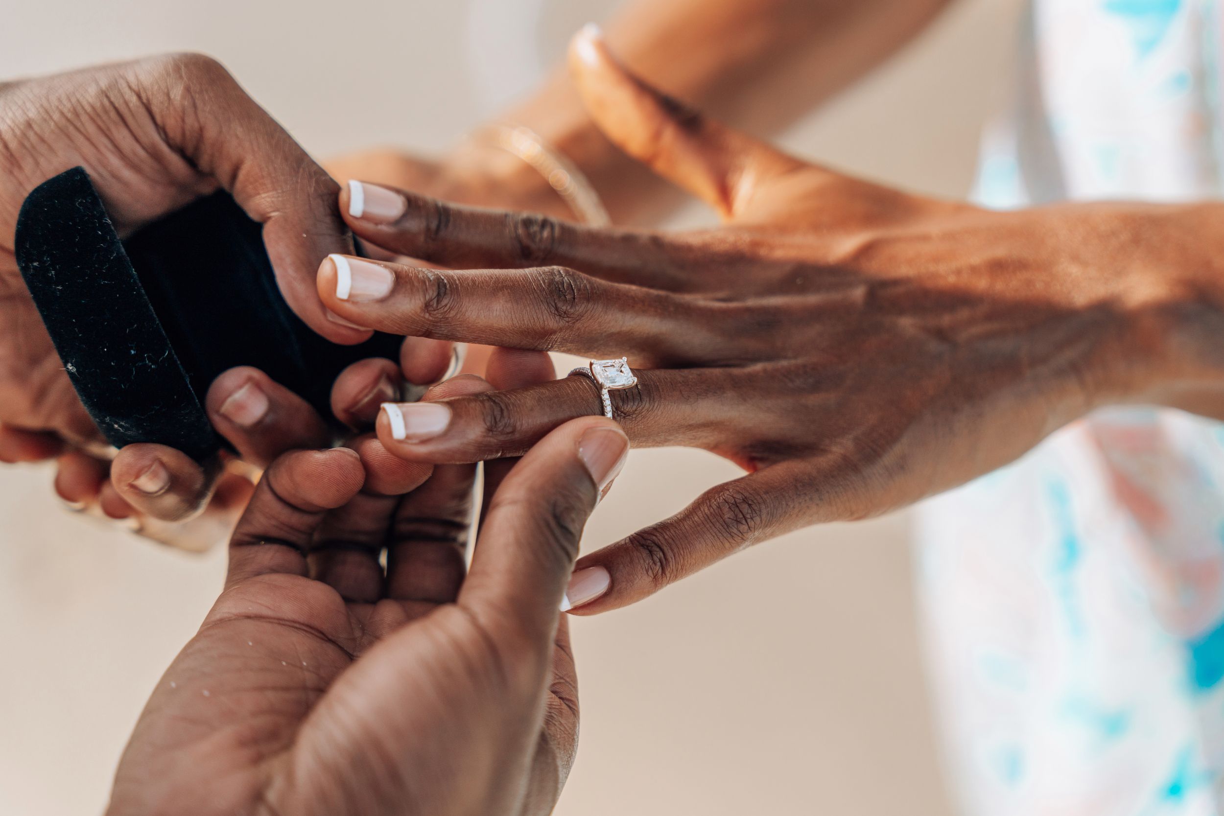Close-up of hands during a ring ceremony, with a diamond engagement ring being placed on a finger.