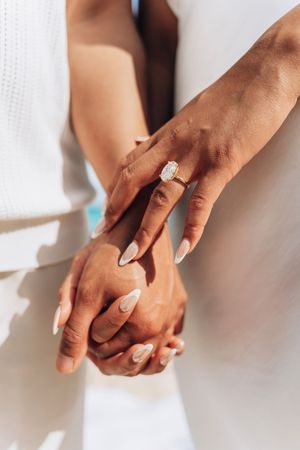 Close-up of couple holding hands showing a stunning emerald cut diamond engagement ring with gold band.