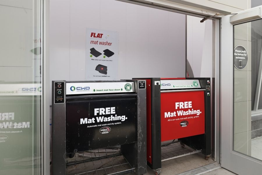 Two red automatic flat mat washing machines offering free mat washing service at a self-service car wash facility.