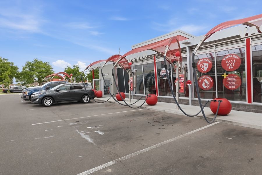 Tommy's Express Car Wash exterior with red circular sculptures and covered drive-through lanes in a sunny parking lot.