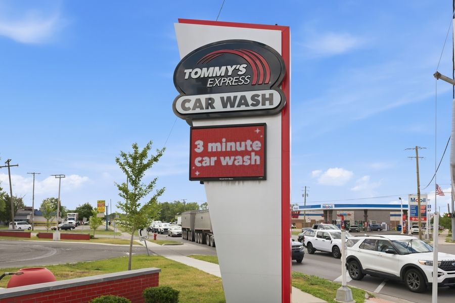 Tommy's Express Car Wash sign advertising a 3-minute car wash service, located in a busy commercial area on a sunny day.