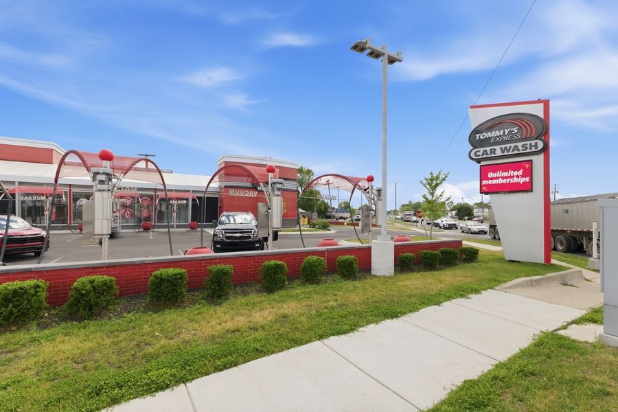Tommy's Express Car Wash facility exterior with drive-through tunnel, red signage, and manicured green lawn.