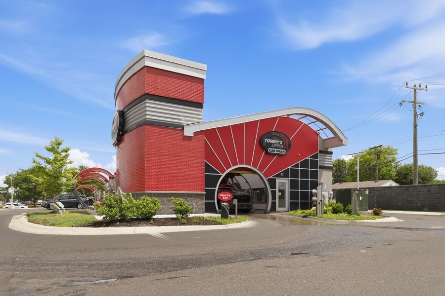 Red and black modern commercial building with curved architectural design, large parking lot, and blue sky background.