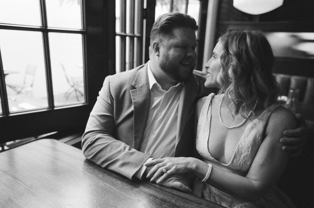 Black and white photo of a smiling couple sitting together at a wooden table in a cozy restaurant booth.