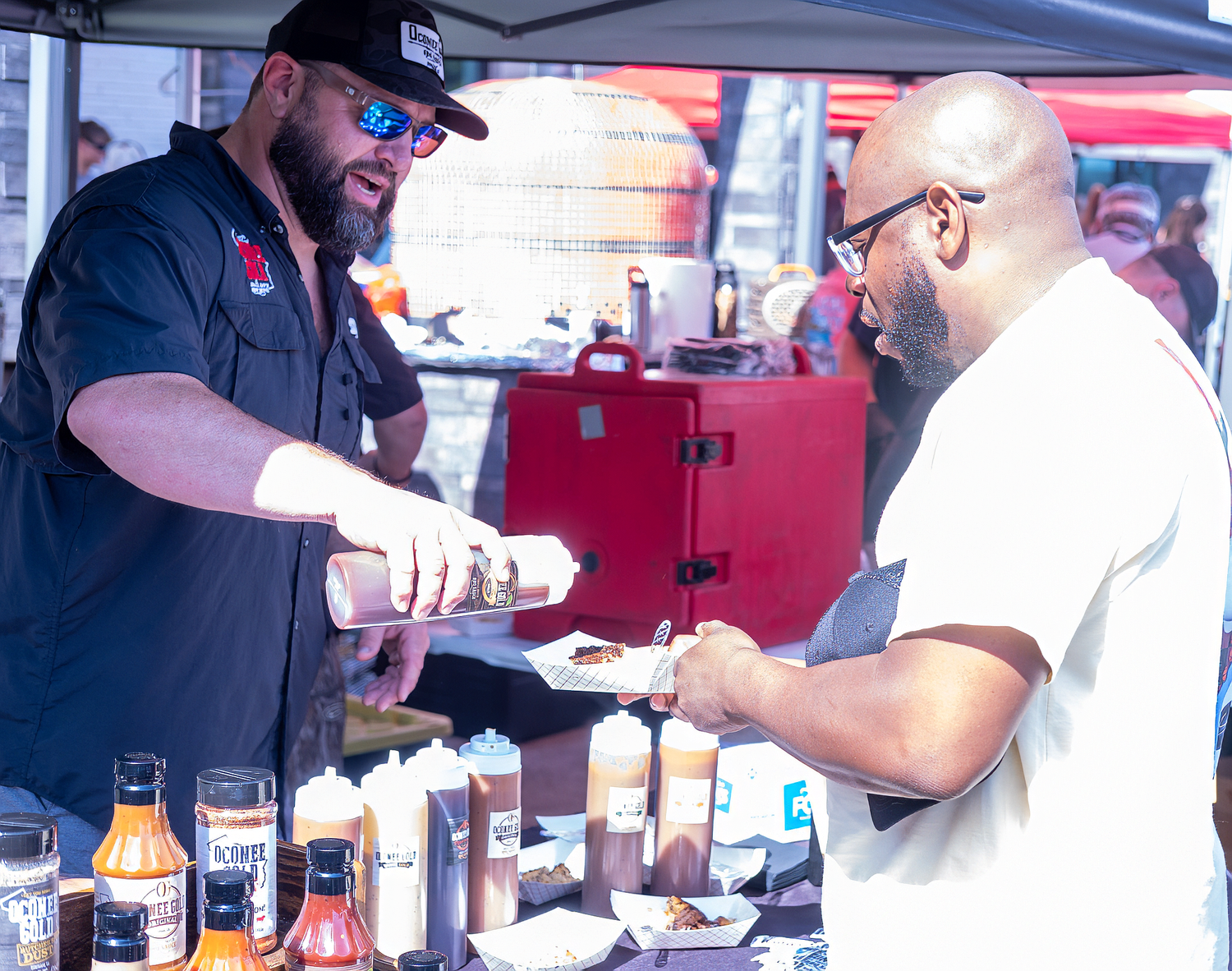 Event picture of vendor serving BBQ samples to a customer at an outdoor food event captured by Nichole Meshad Photography.