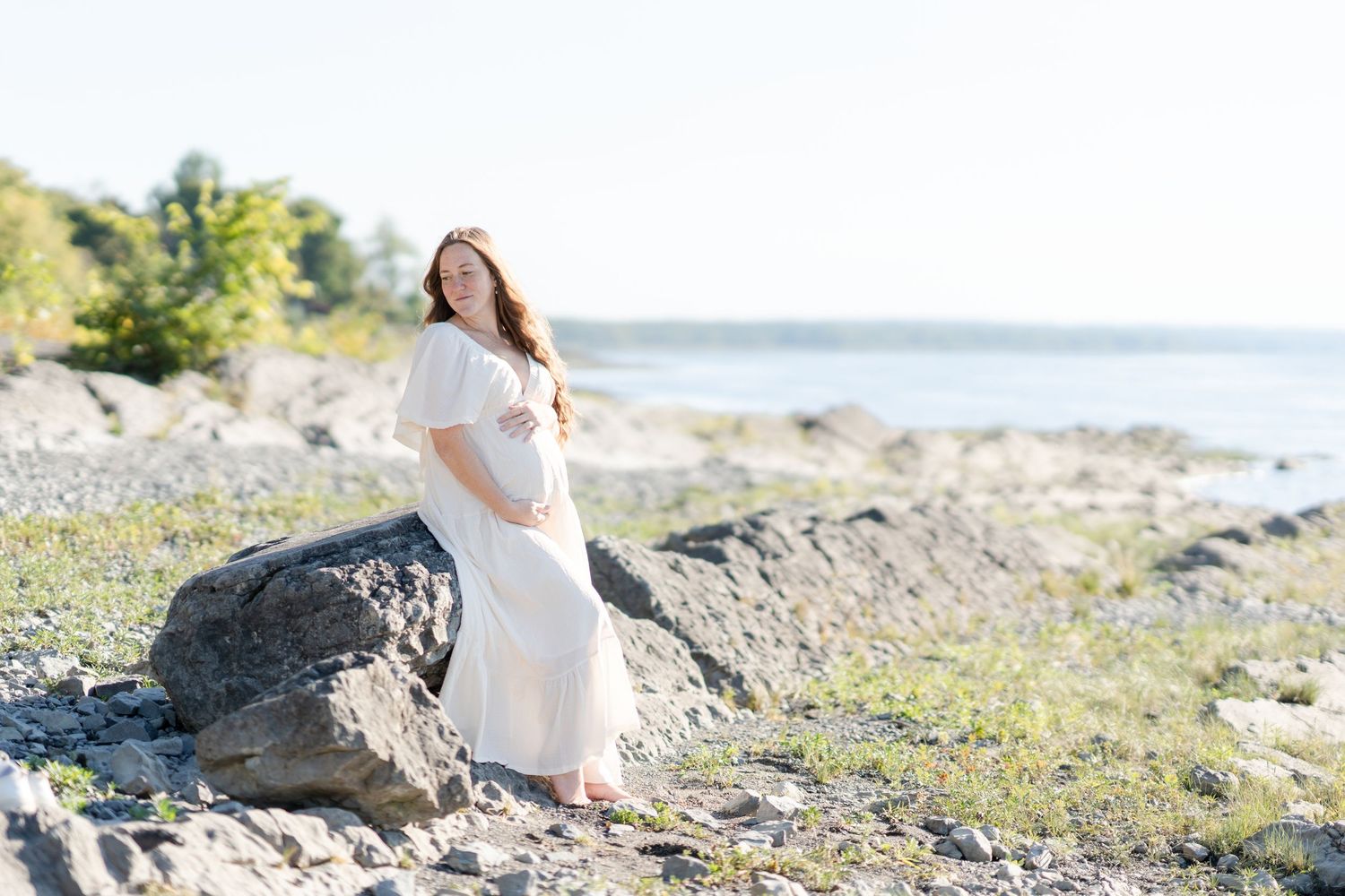 Future maman dans une robe blanche et vaporeuse sur la plage de Neuville pour sa séance photo de maternité dans la région de Portneuf