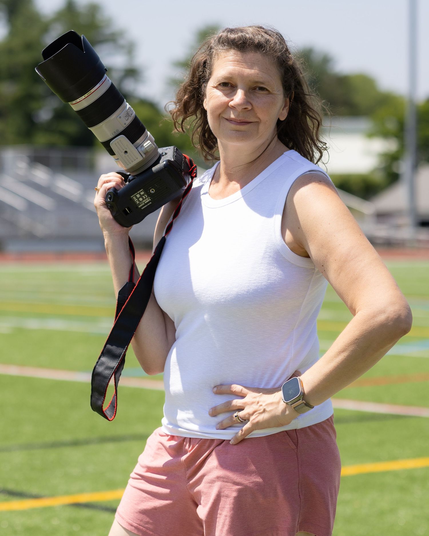 Portrait of photographer Laura Lavoie holding a Canon camera on a sports field.