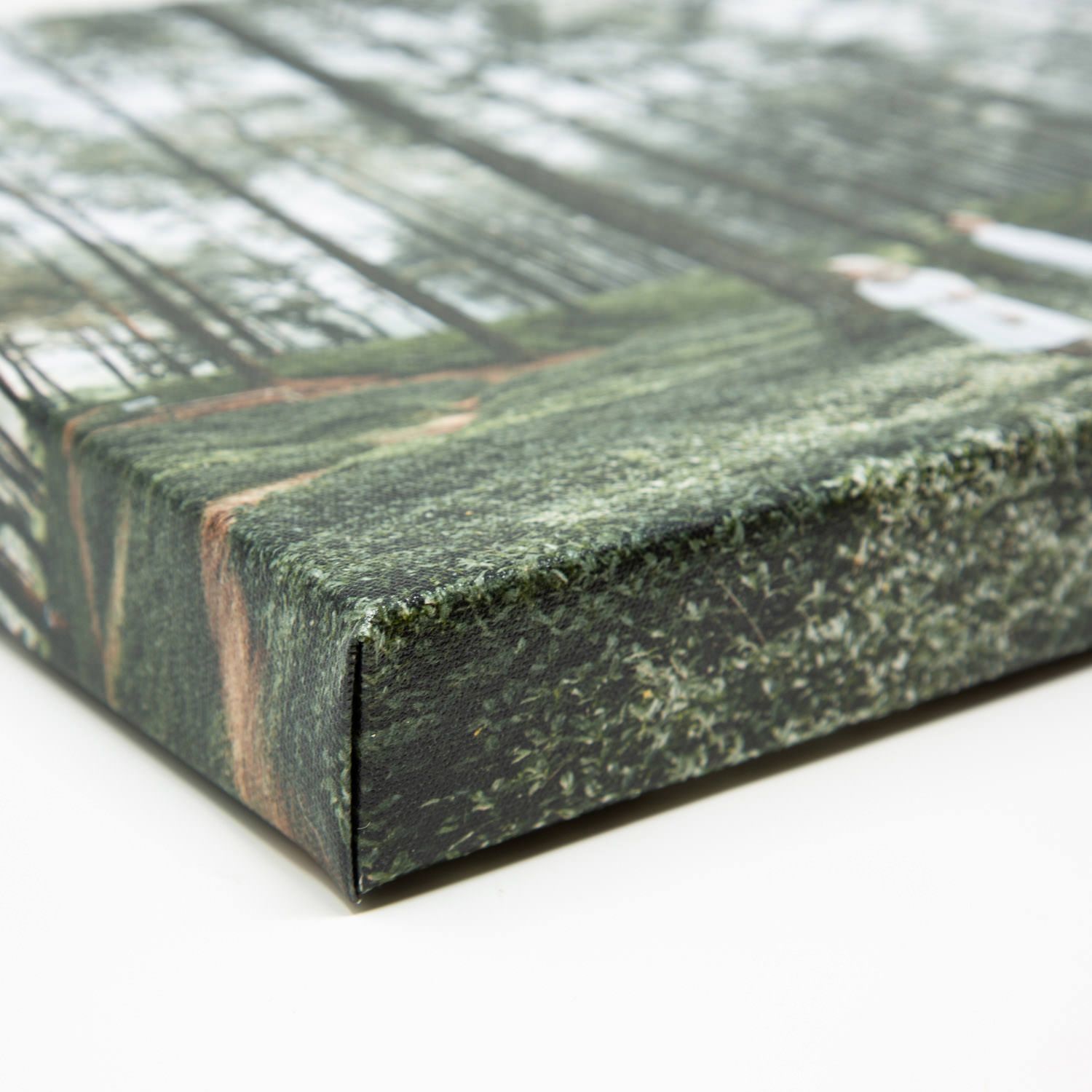 Close-up corner detail of a wrapped canvas print featuring a moody green forest landscape.