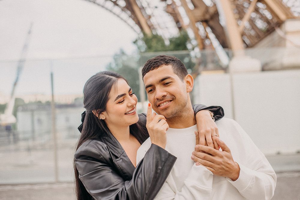 A happy couple embraces near the Eiffel Tower in Paris, sharing a tender romantic moment outdoors.