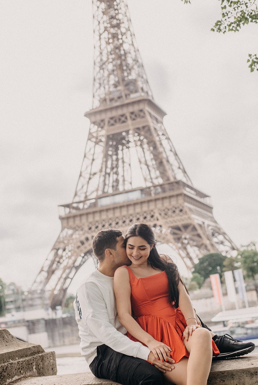 Couple sitting together in front of the Eiffel Tower in Paris, woman in red dress smiling.