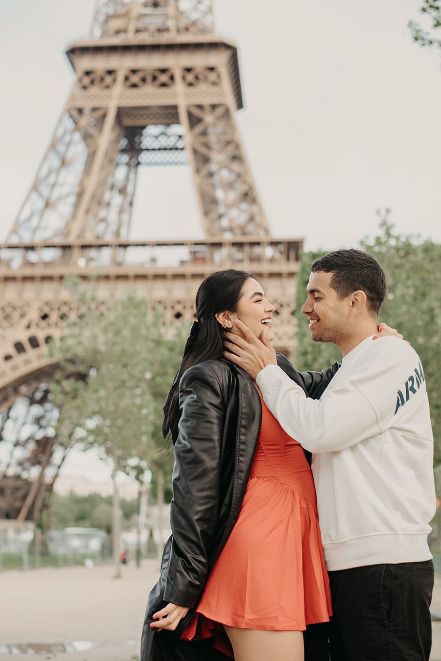 A couple embraces and smiles at each other in front of the Eiffel Tower in Paris, France.