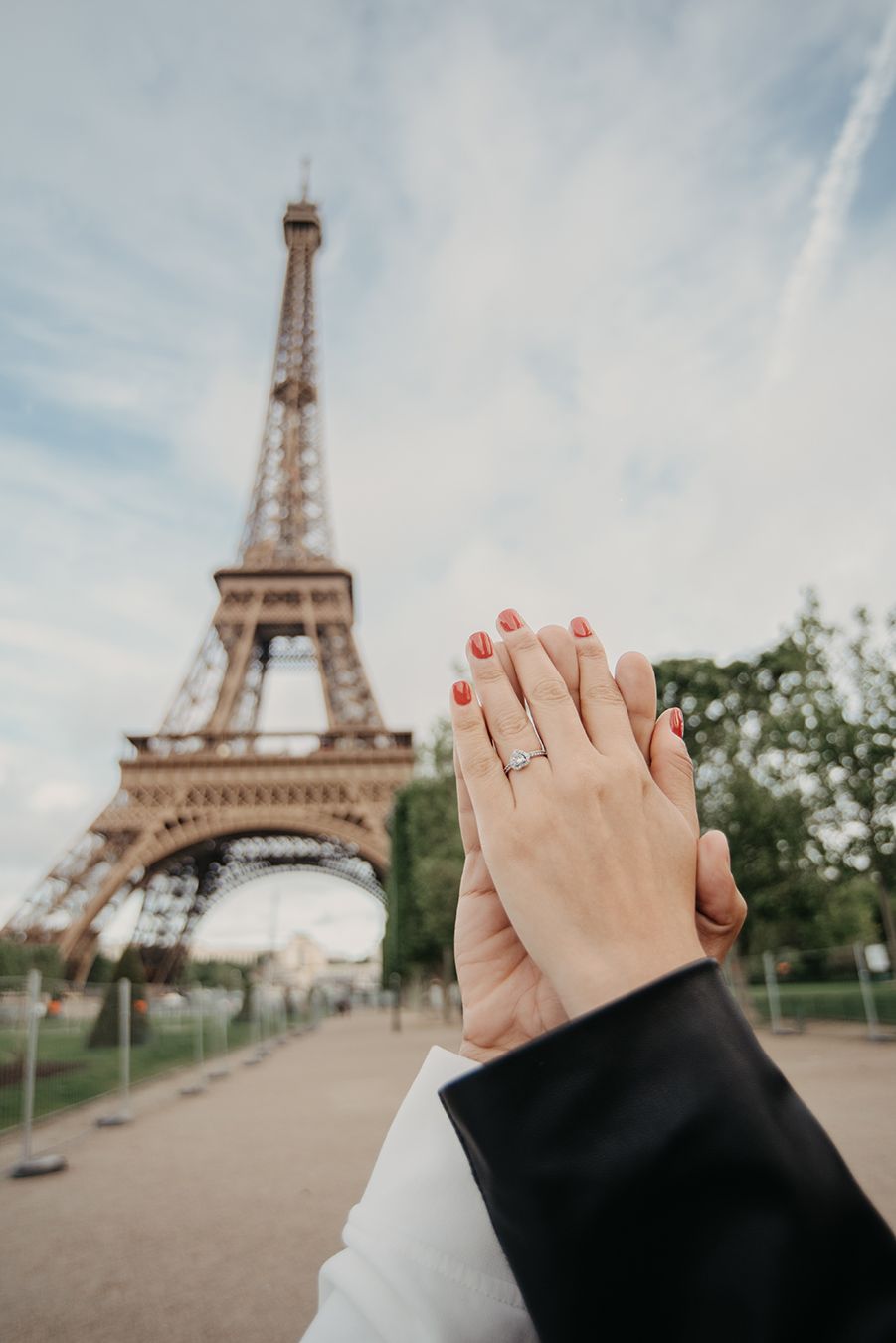 Couple showing engagement ring with diamond in front of the Eiffel Tower in Paris, France.