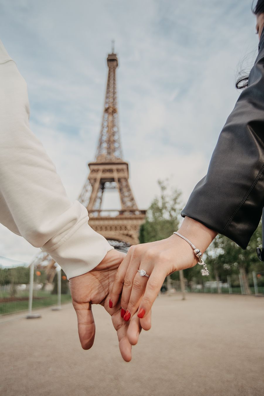 Couple holding hands with engagement ring in front of the Eiffel Tower in Paris, France.
