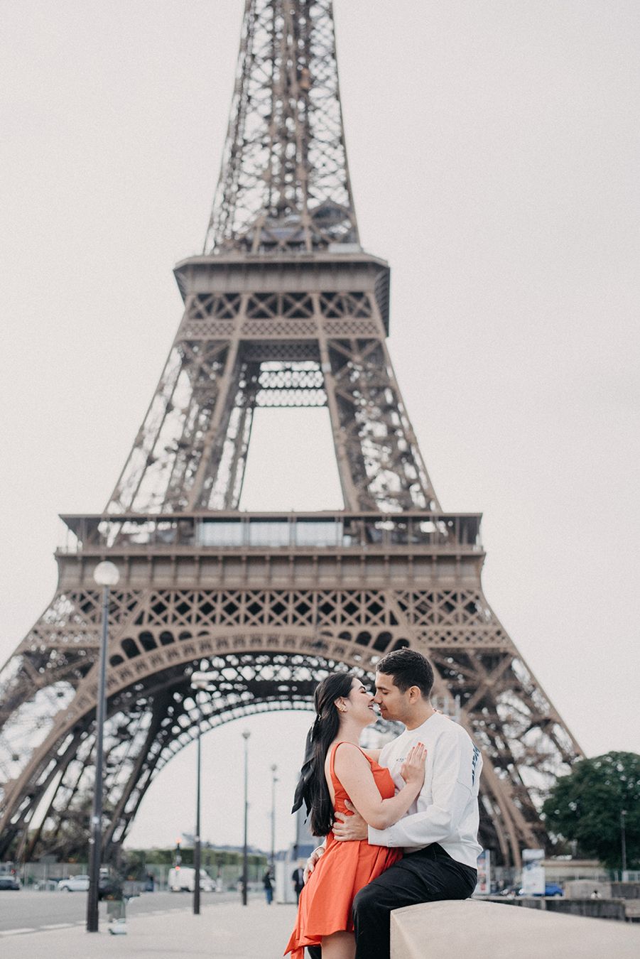 Romantic couple embracing in front of the Eiffel Tower in Paris, woman in red dress, man in white shirt.