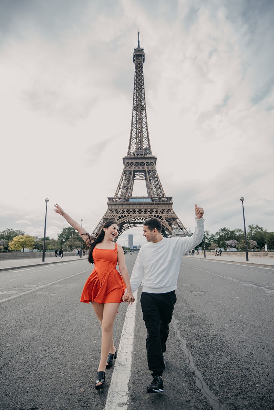Couple holding hands and dancing on a road in front of the Eiffel Tower in Paris, woman in red dress.