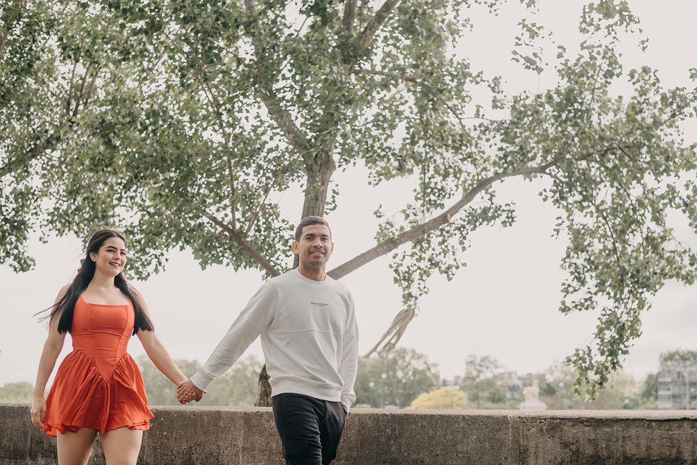 Happy couple holding hands and walking together under a large green tree outdoors.