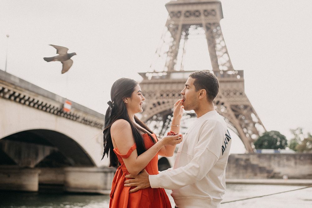 Couple embracing near the Eiffel Tower in Paris with a bird flying overhead on a romantic day.