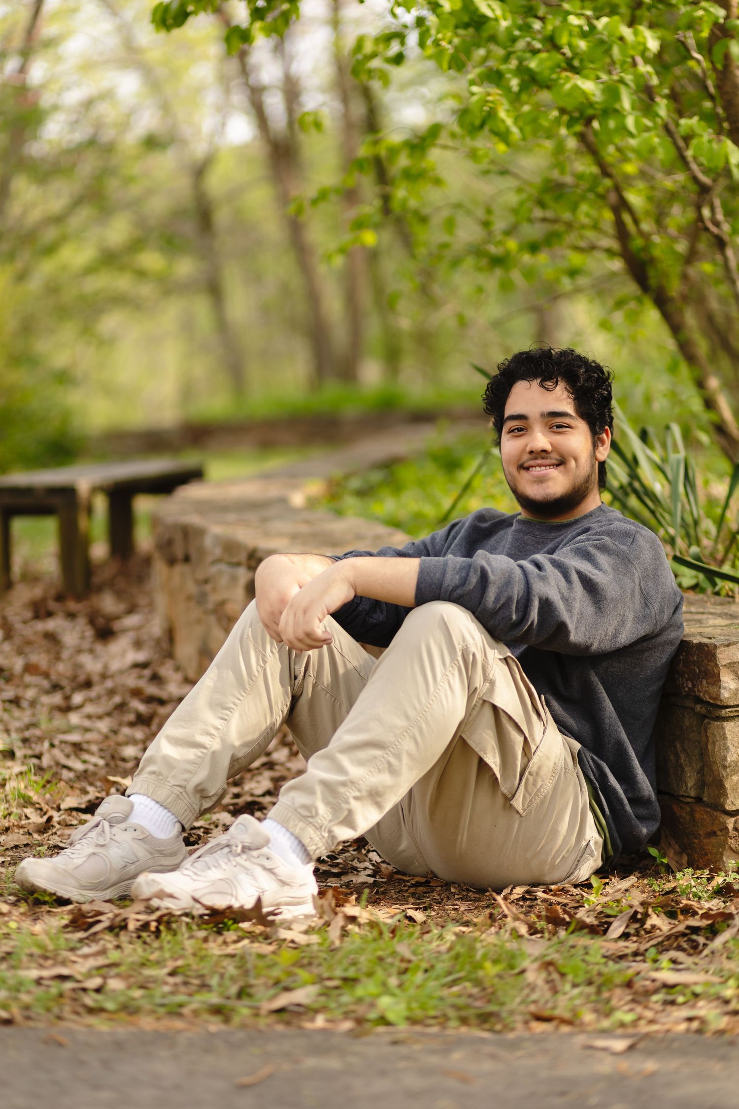 Young with dark hair sits against a stone wall for his senior session at Ivy Natural area, captured by Charlottesville family photographer.