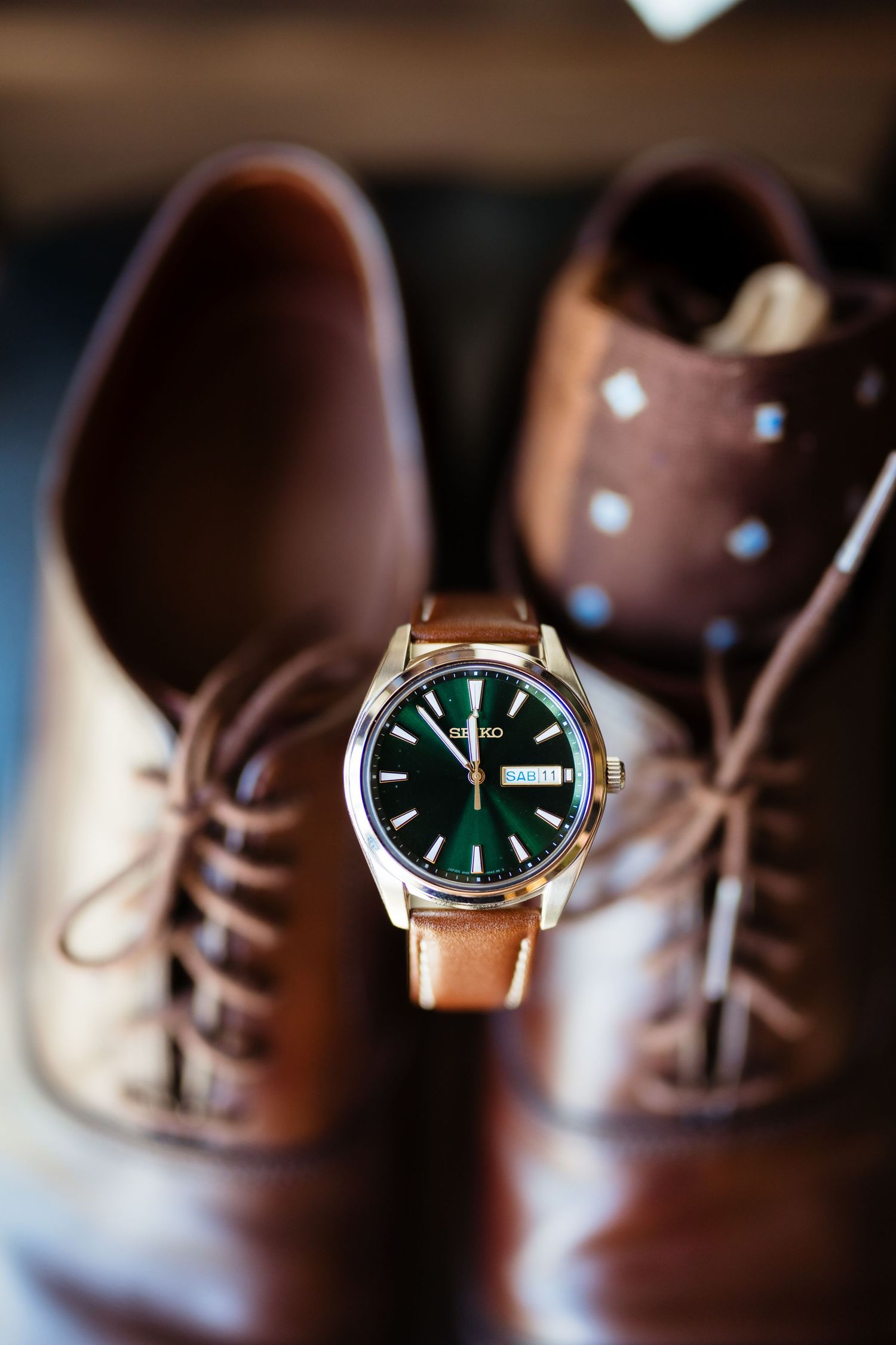 Seiko watch with green dial and tan leather strap displayed between brown leather oxford dress shoes.