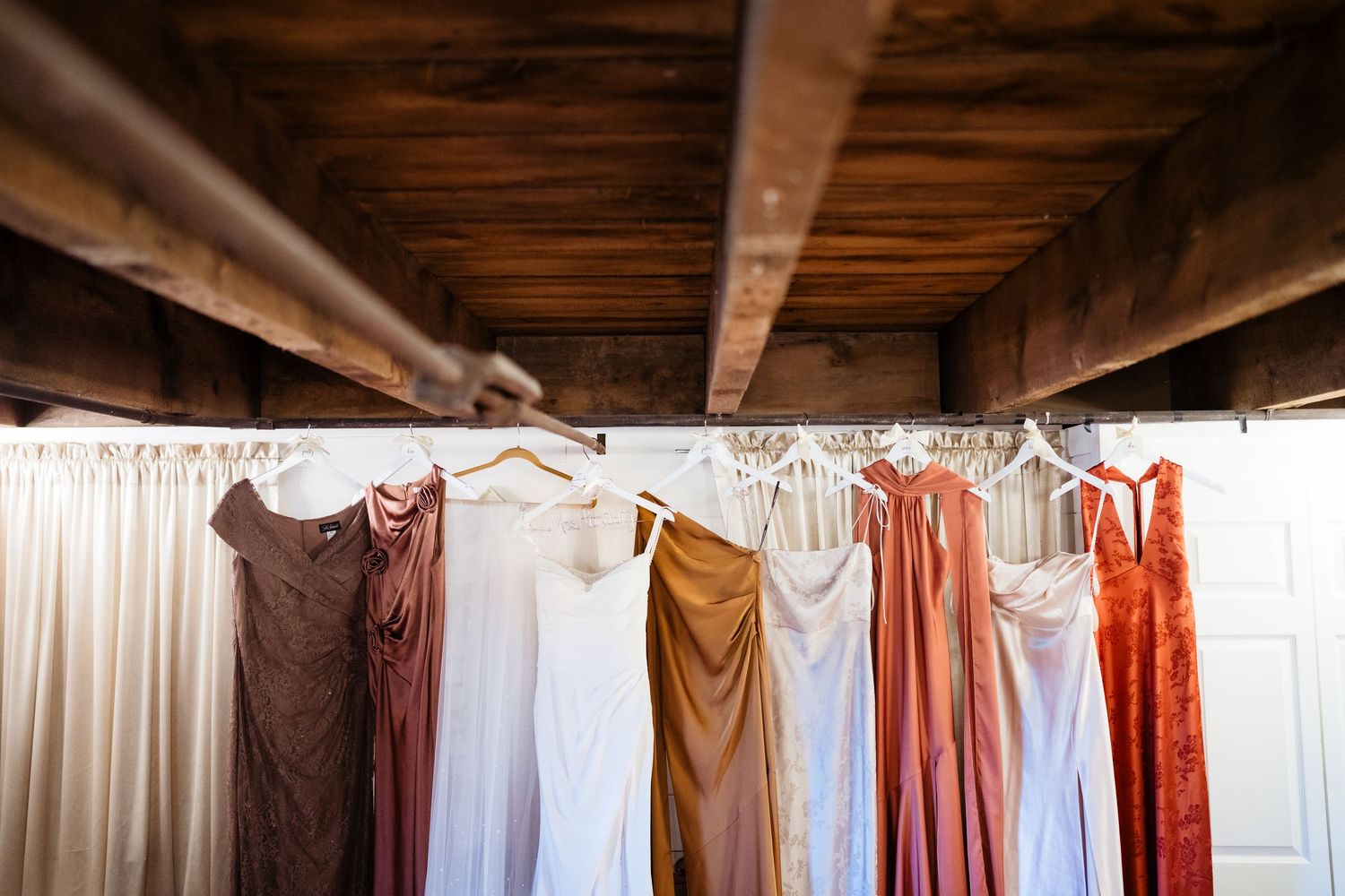 Colorful bridesmaid dresses hanging on a rustic wooden rack in a barn wedding venue.