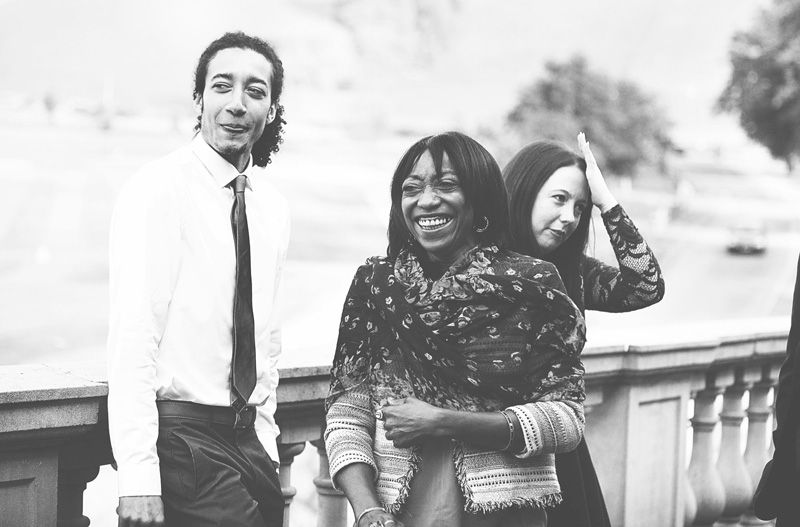 Black and white photo of three friends smiling and posing together outdoors near a decorative stone railing.