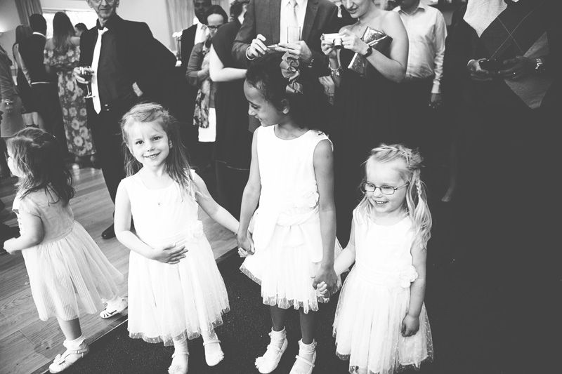 Black and white photo of young flower girls in white dresses holding hands at a wedding reception.