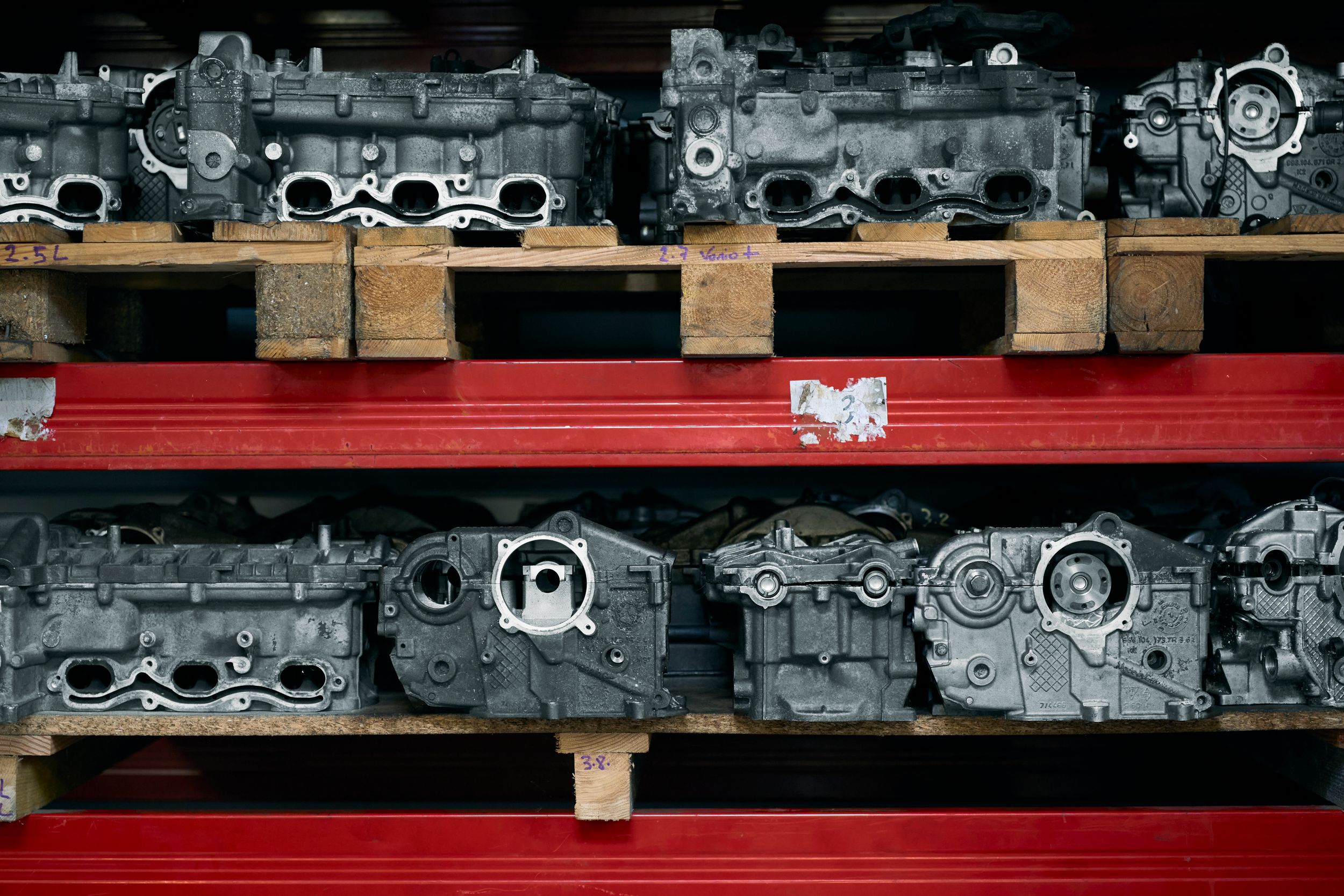 Multiple used engine cylinder heads stored on wooden pallets on red metal shelving racks.