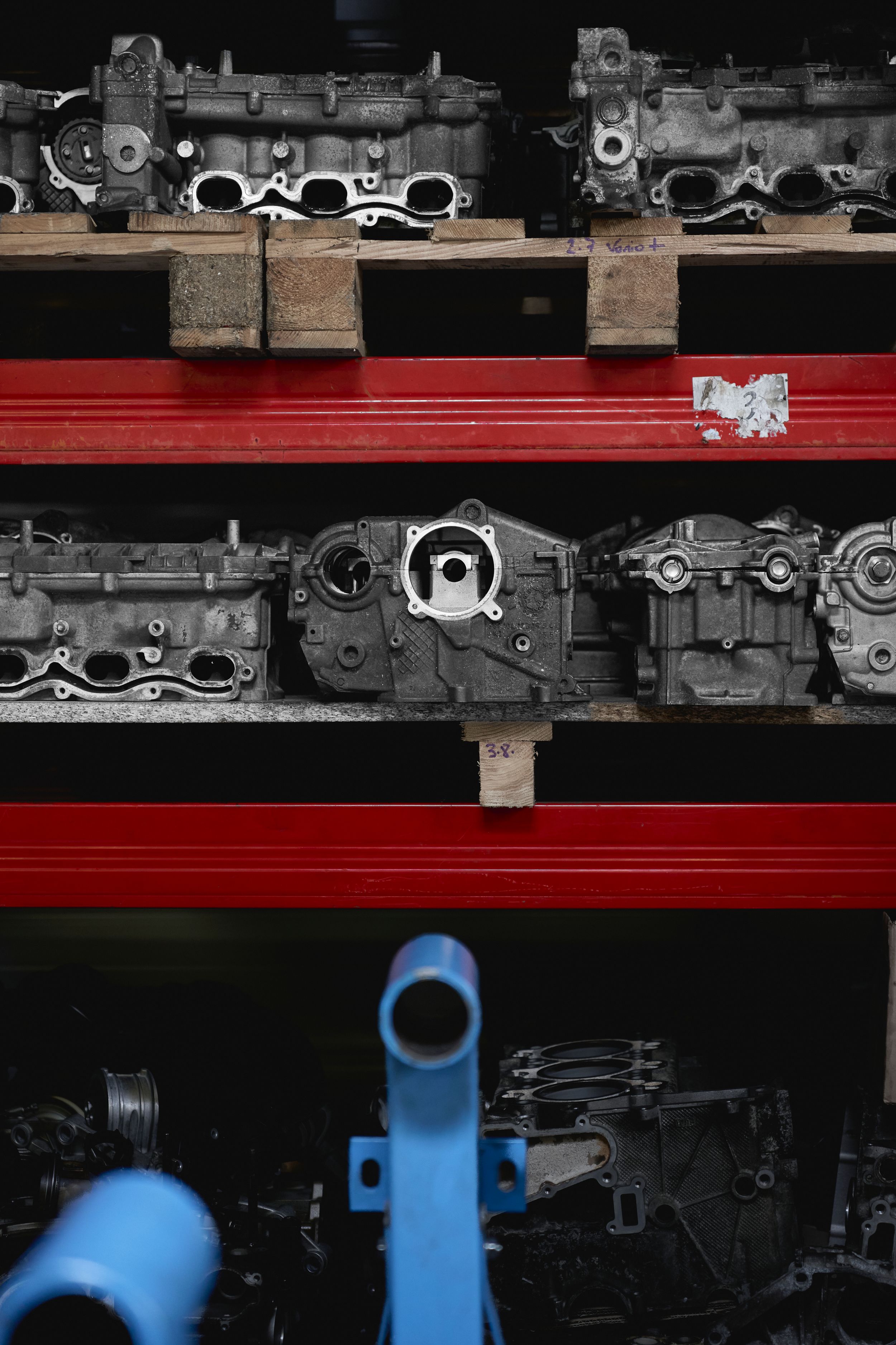 Used automotive engine blocks and cylinder heads stored on red metal shelving in a workshop.