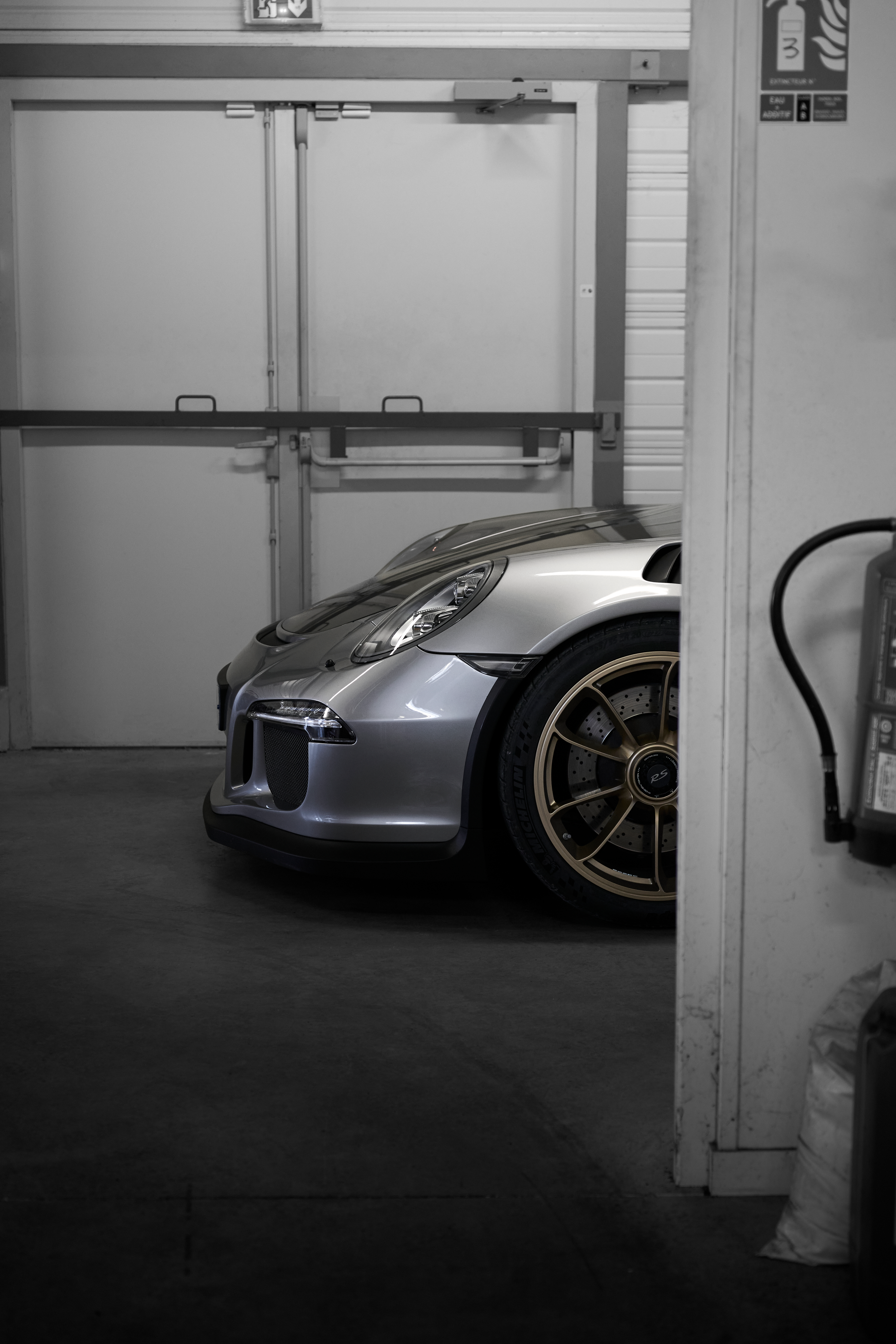 Silver Porsche 911 GT3 RS with gold wheels partially visible through a garage doorway.