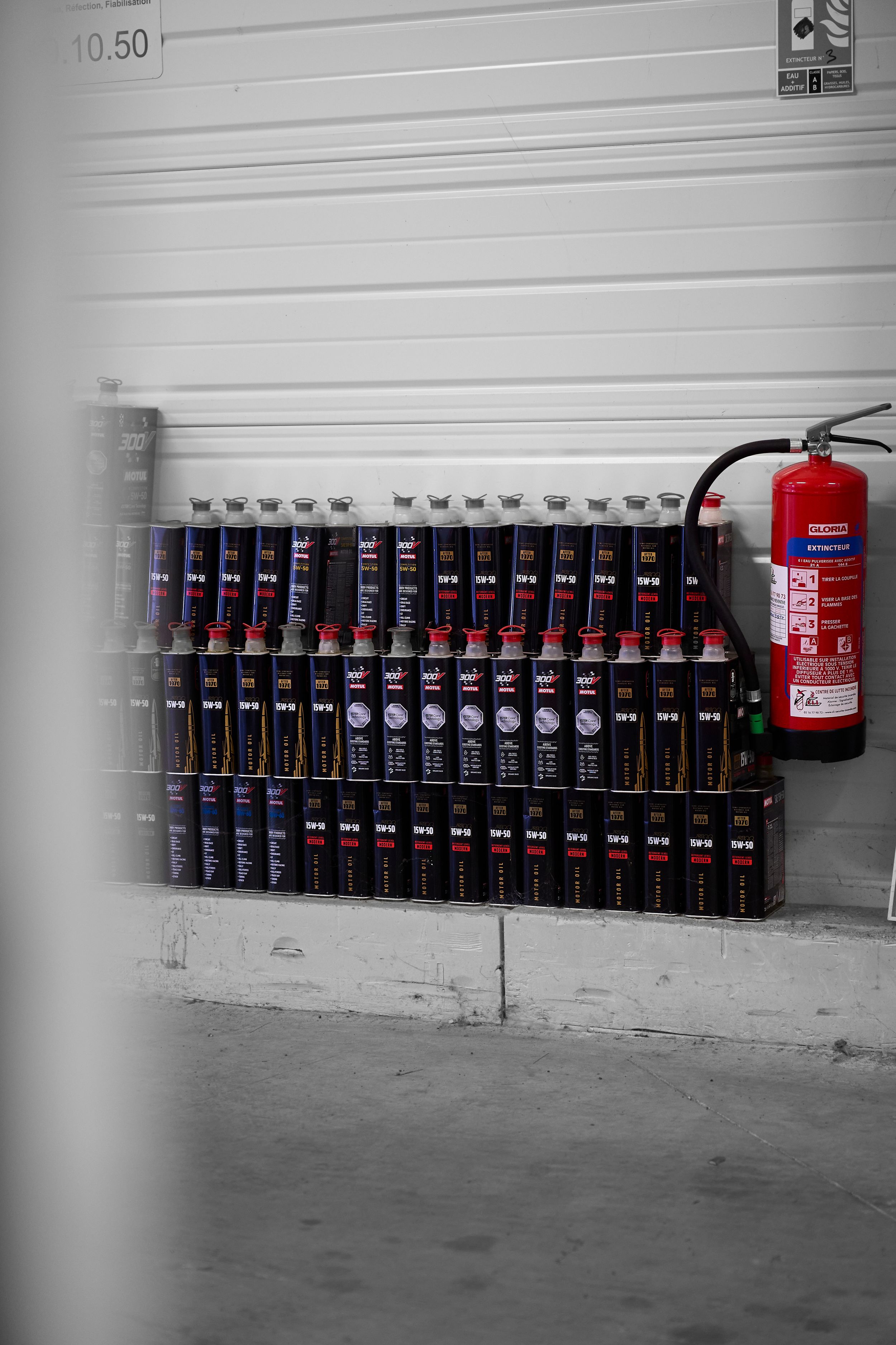 Rows of automotive lubricant cartridges stacked against a wall beside a red fire extinguisher.