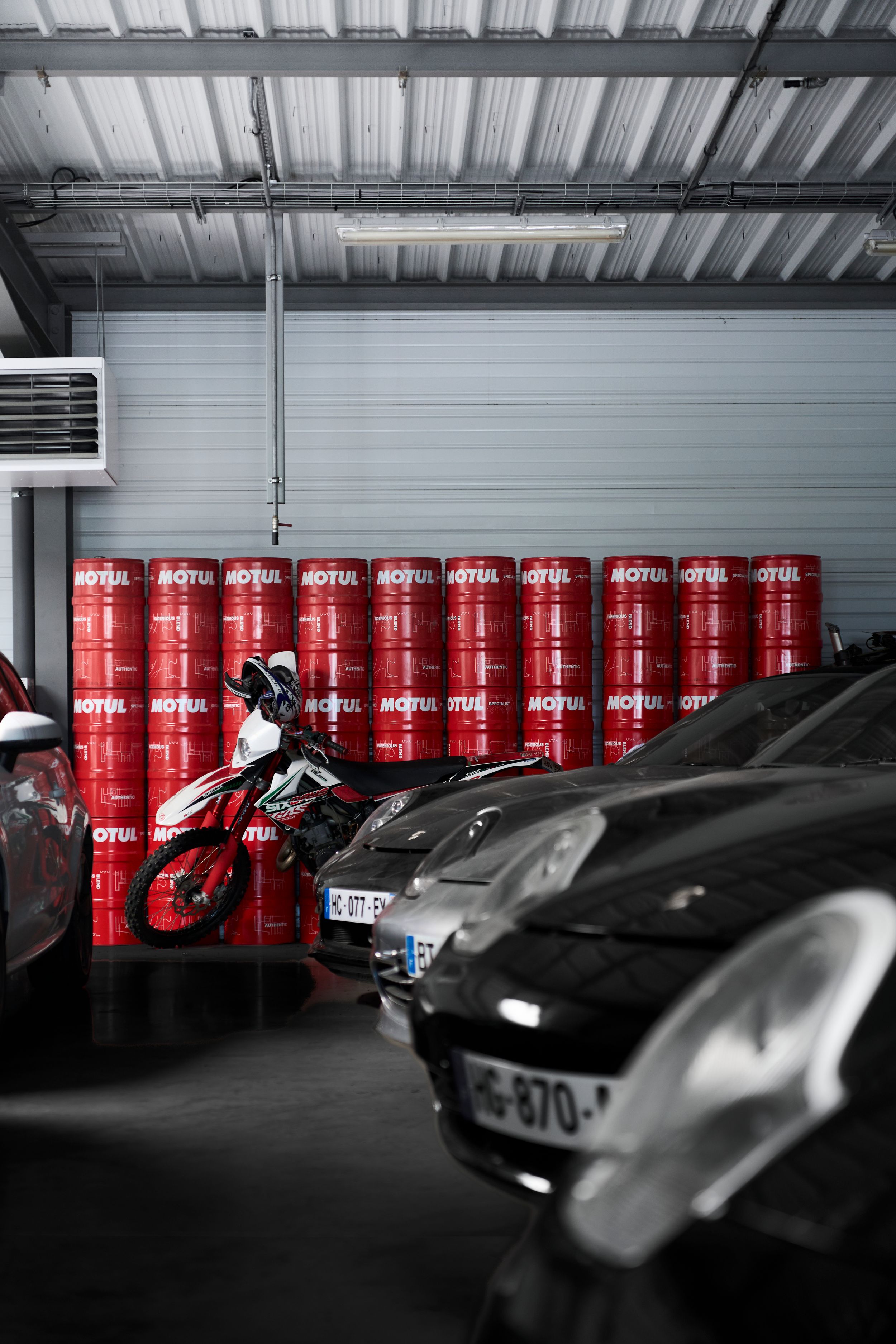 Motul oil drums lined against garage wall with cars and a motorcycle parked inside.