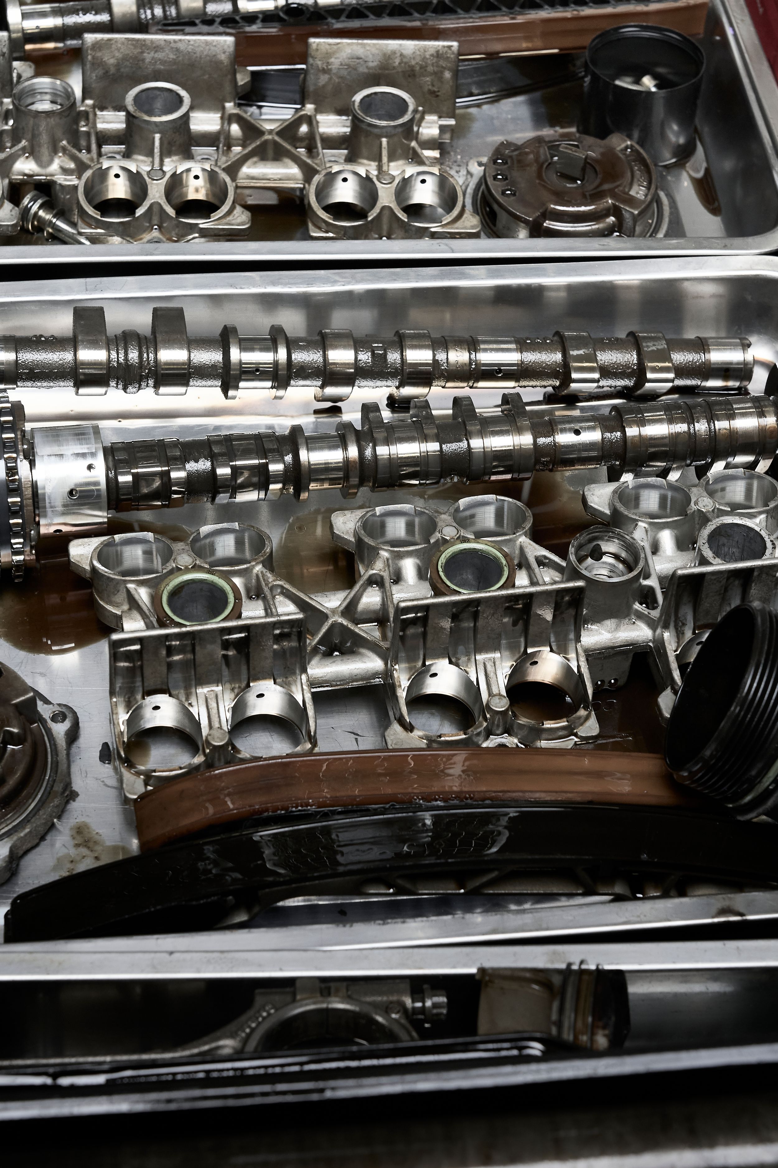 Disassembled engine components including camshafts and pistons laid out in a metal tray.