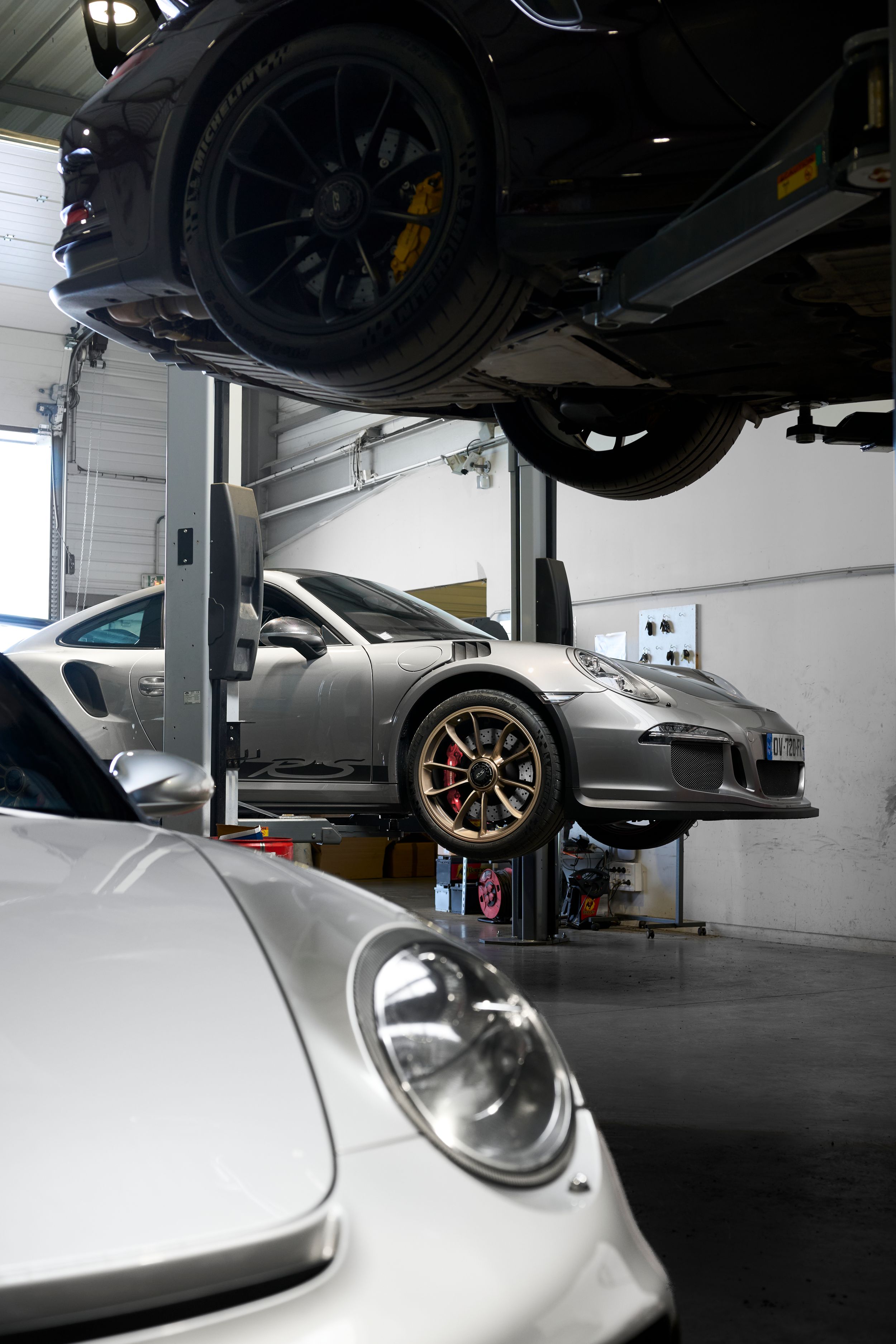 Multiple Porsche 911 sports cars on hydraulic lifts inside a professional automotive service center.