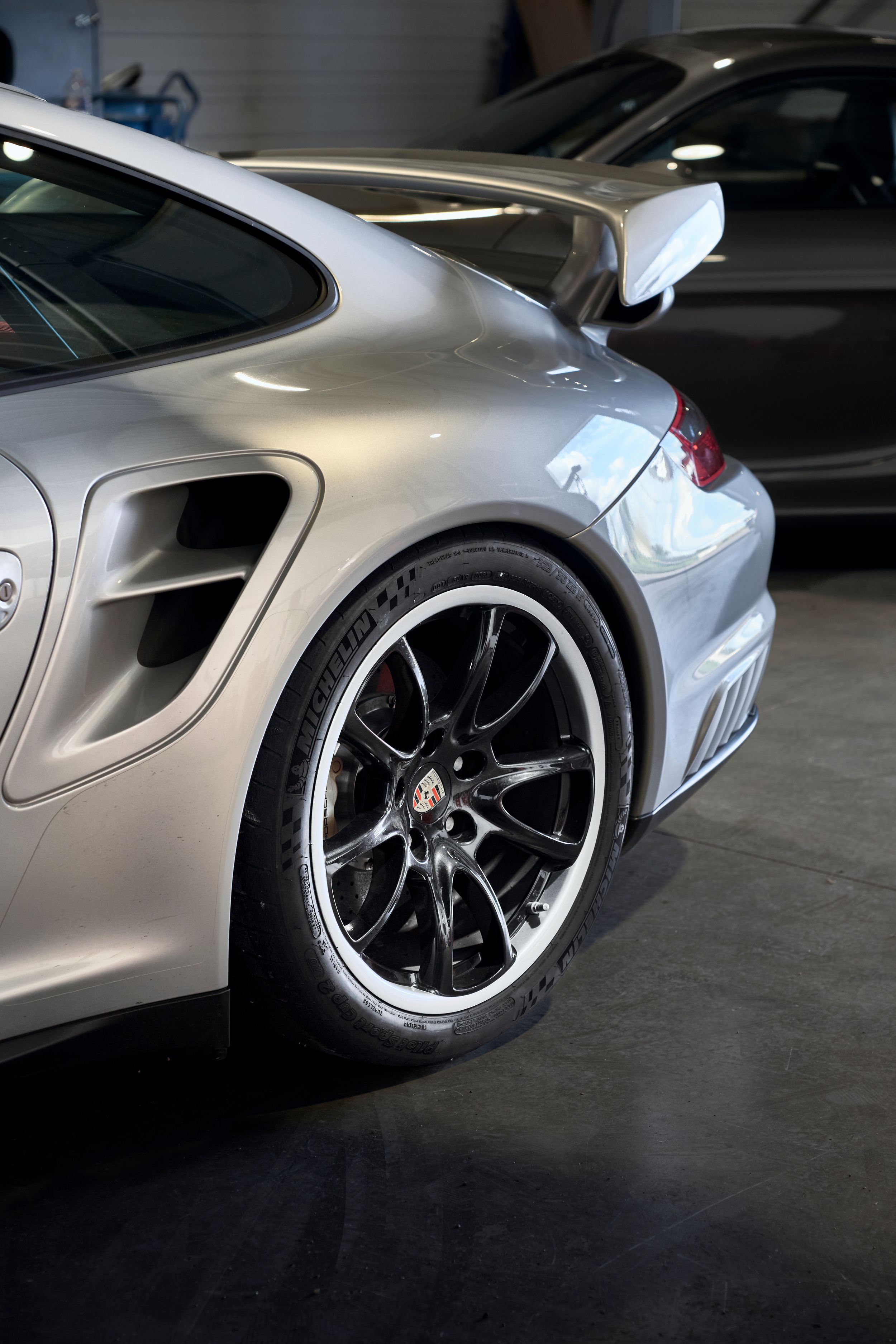 Close-up of silver Porsche 911 GT3 rear wheel arch with black alloy wheel and wide body kit.