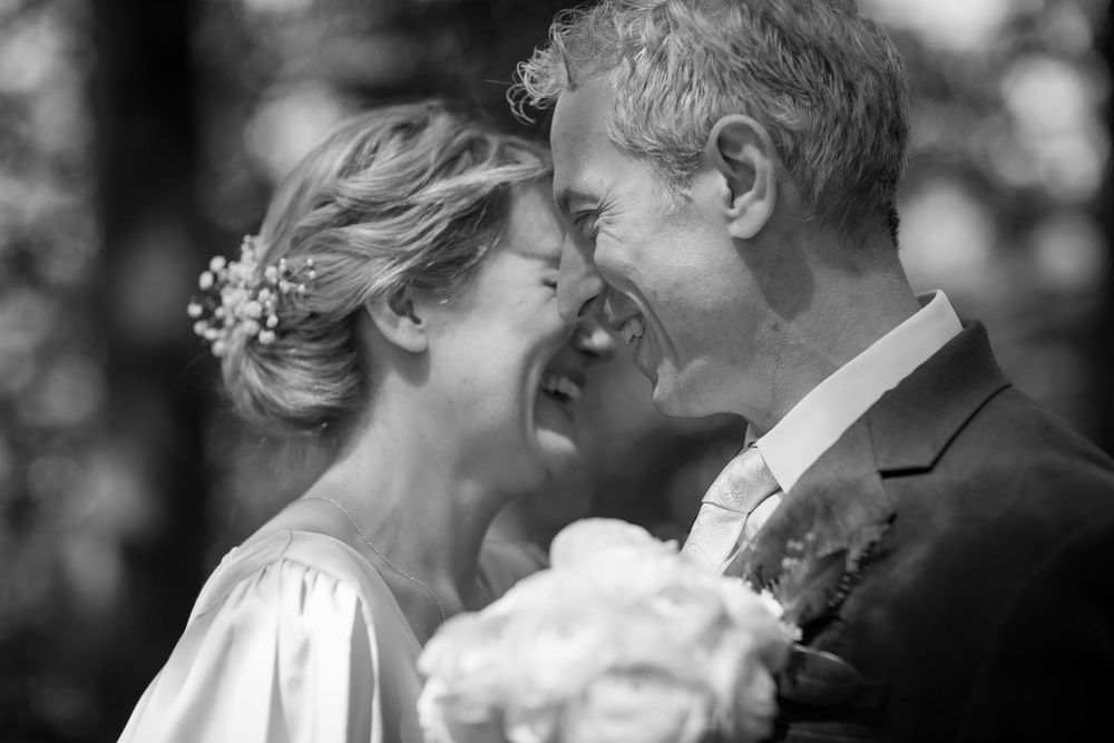 Black and white wedding photo of smiling bride and groom leaning foreheads together, bride holding white bouquet.
