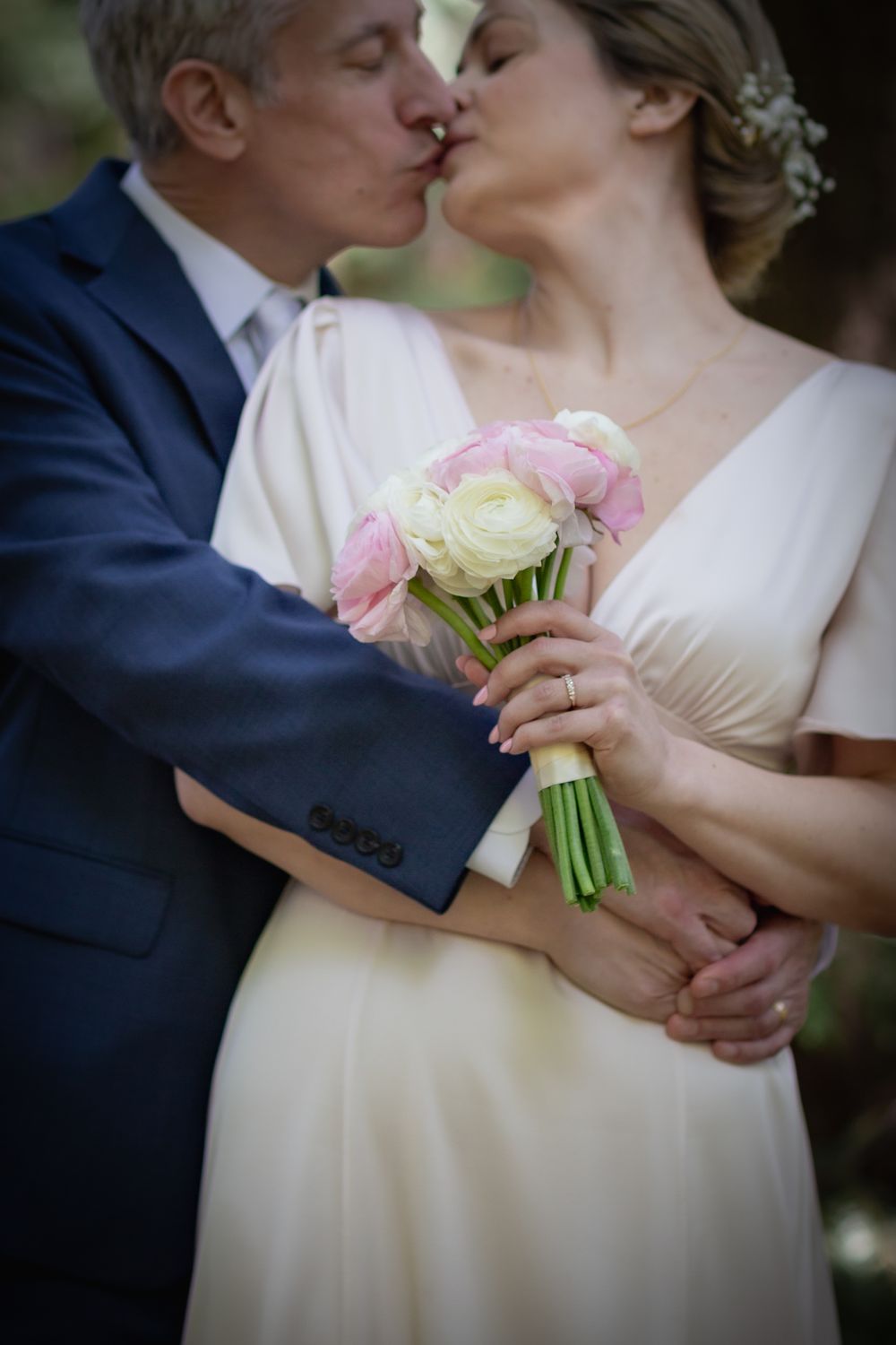 A bride and groom share a kiss while holding a bouquet of pink and white roses at their wedding.