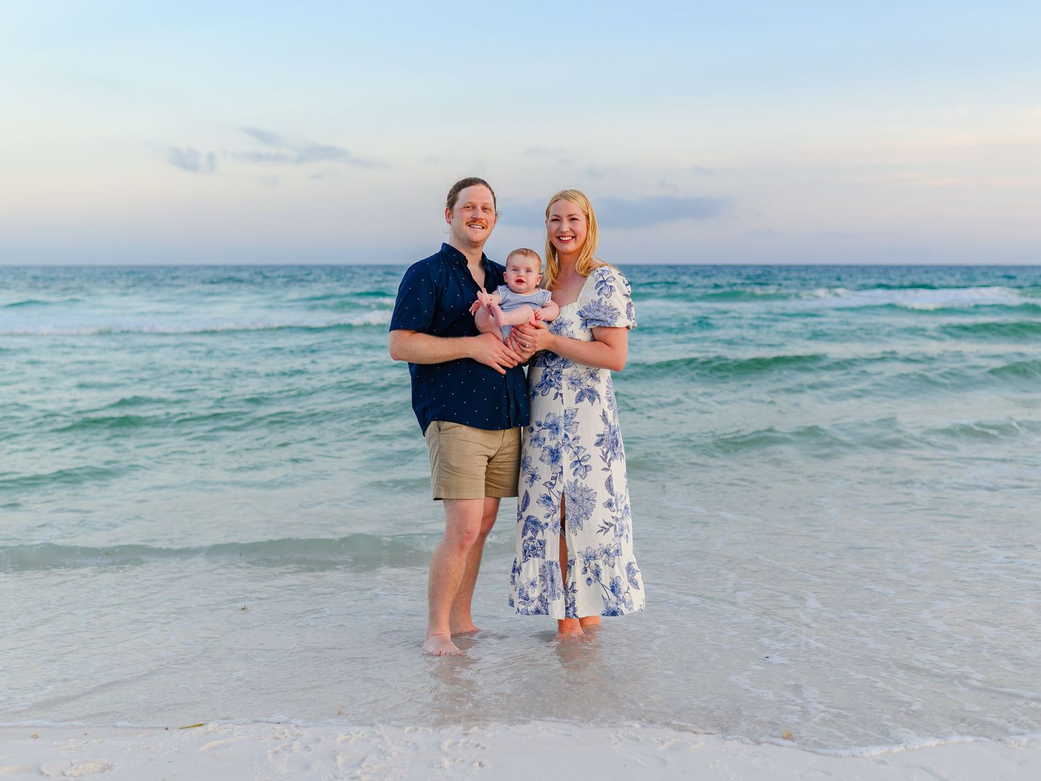A happy family with a baby posing together on a beautiful sandy beach at sunset.