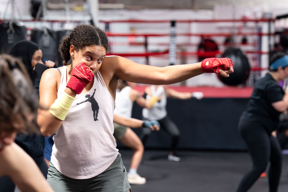 Woman in boxing gloves throwing a jab during a group class.